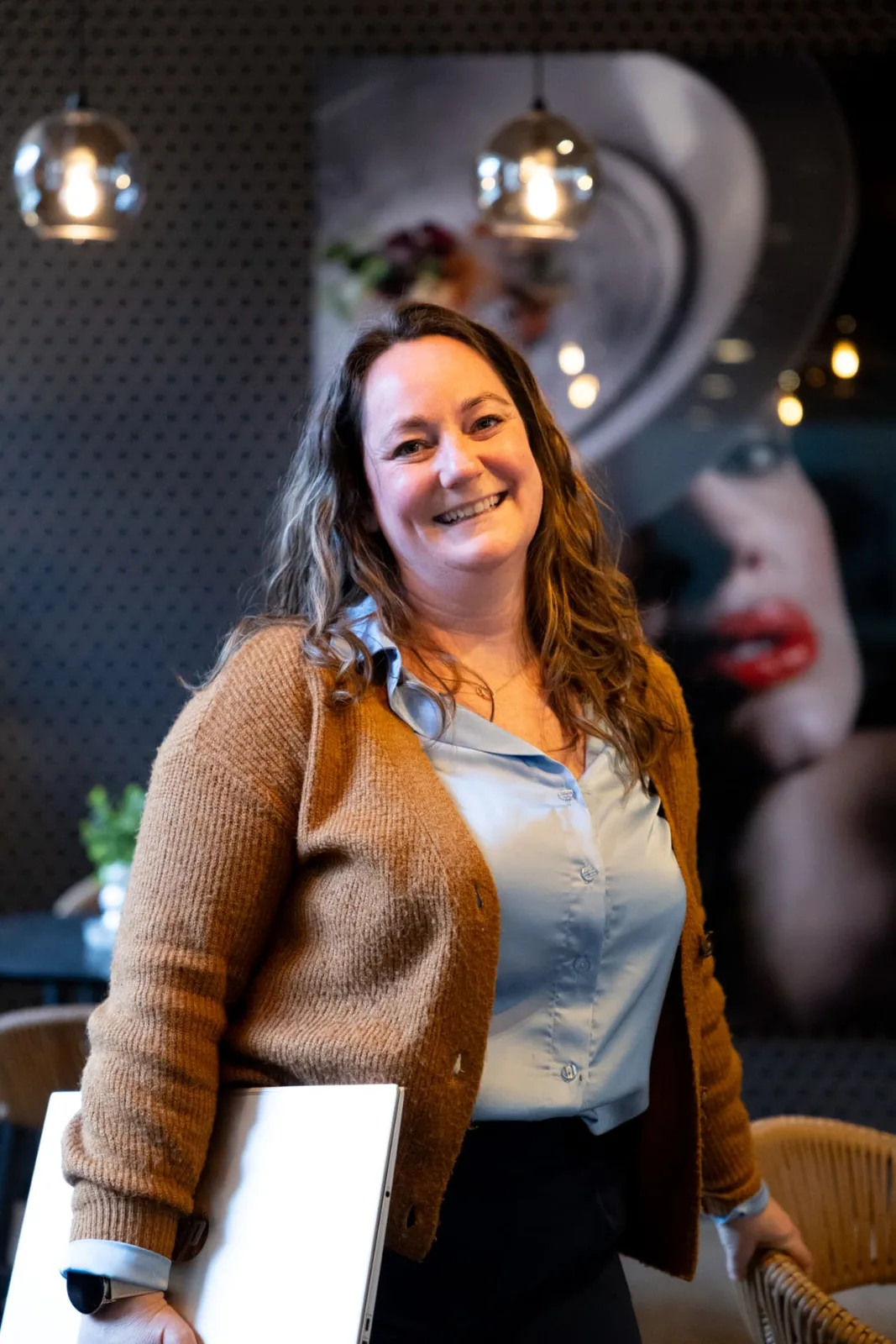 Annelies Neven staat glimlachend met haar laptop onder de arm in een café