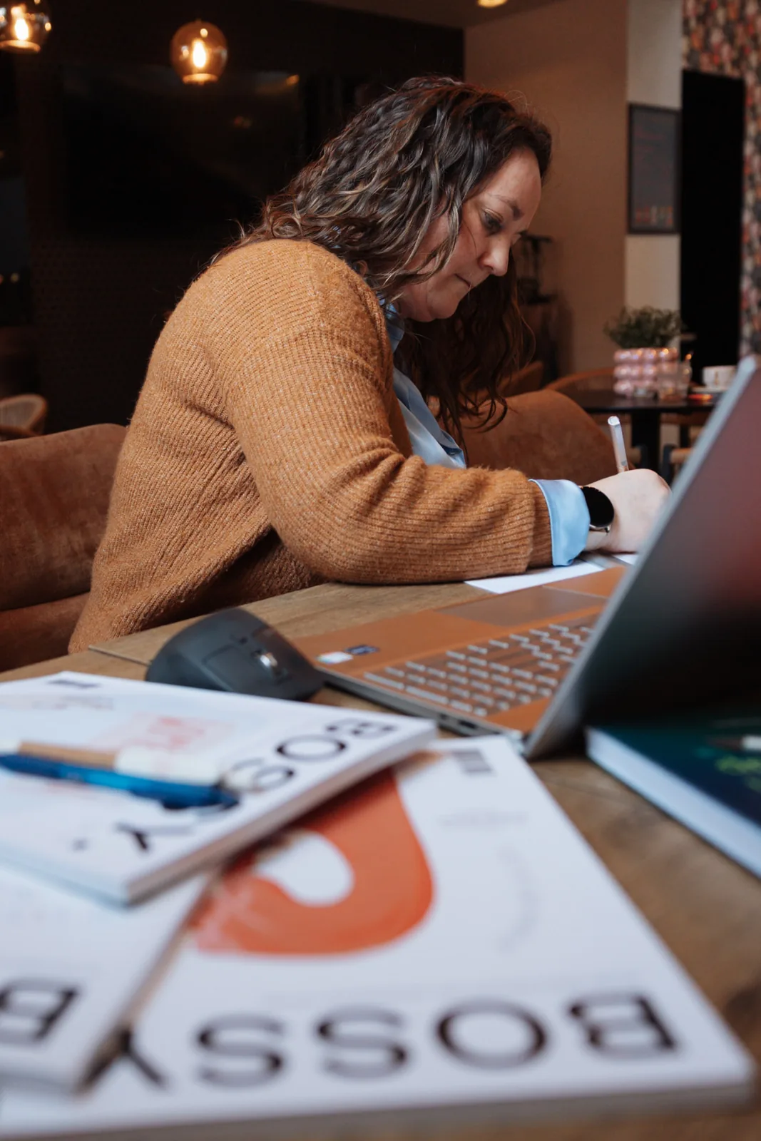 Annelies aan het schrijven aan de laptop, warme oker cardigan