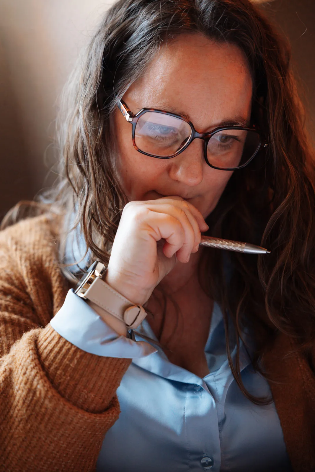 Annelies met bril en pen aan de lippen, in gedachten verzonken