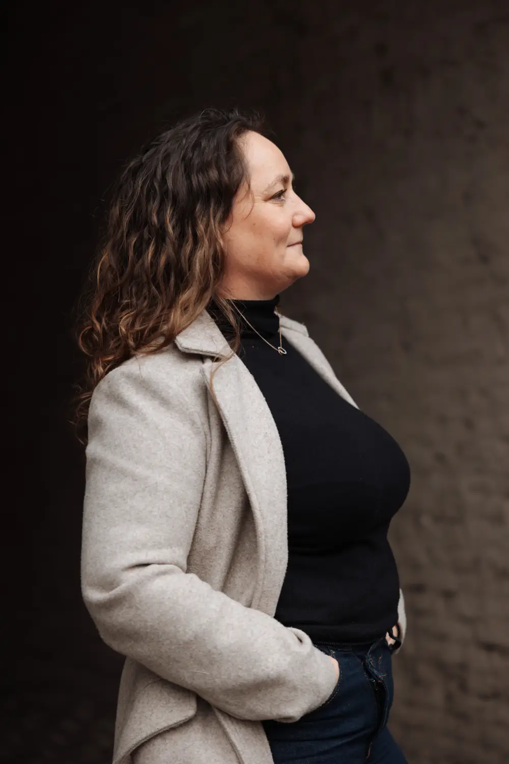 Annelies Neven in zijaanzicht met een beige mantel, blik vooruit