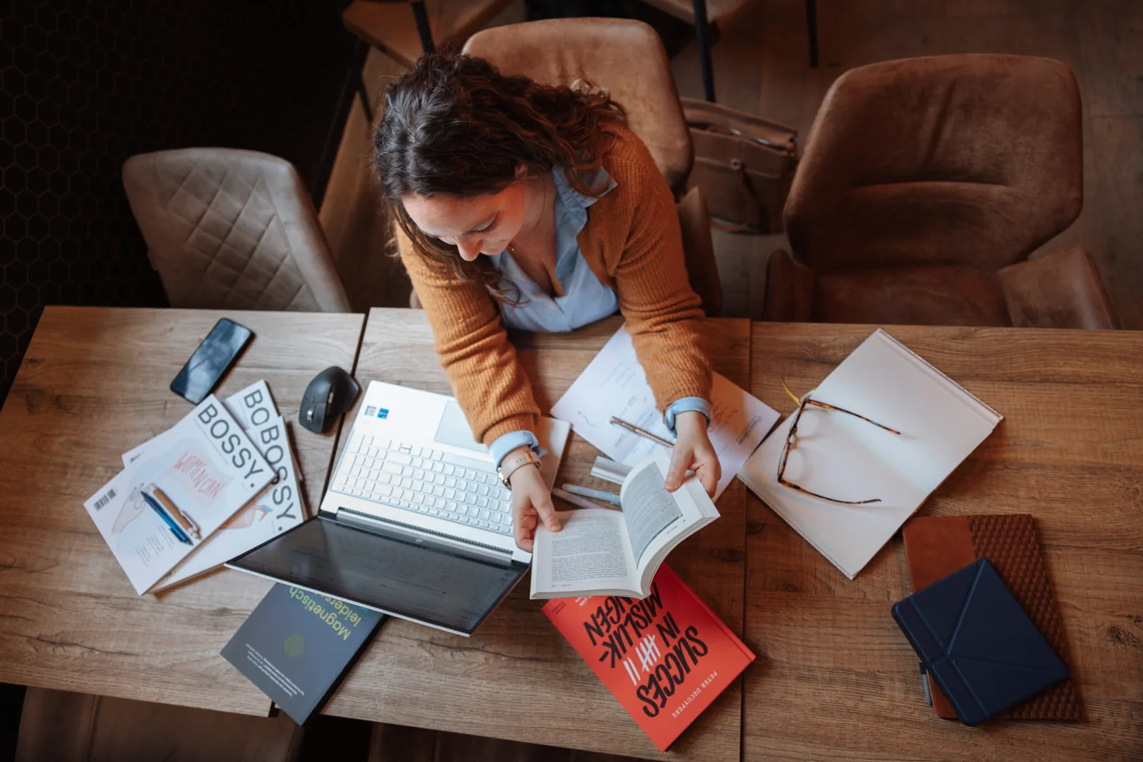 Bovenaanzicht van Annelies aan een werktafel met laptop, boeken en notities